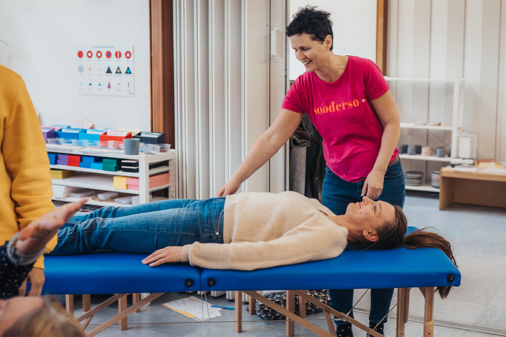 Seminarteilenehmer bei den praktischen Übungen. Im Fokus 2 Frauen. Einer auf der Liege, eine als Trainerin