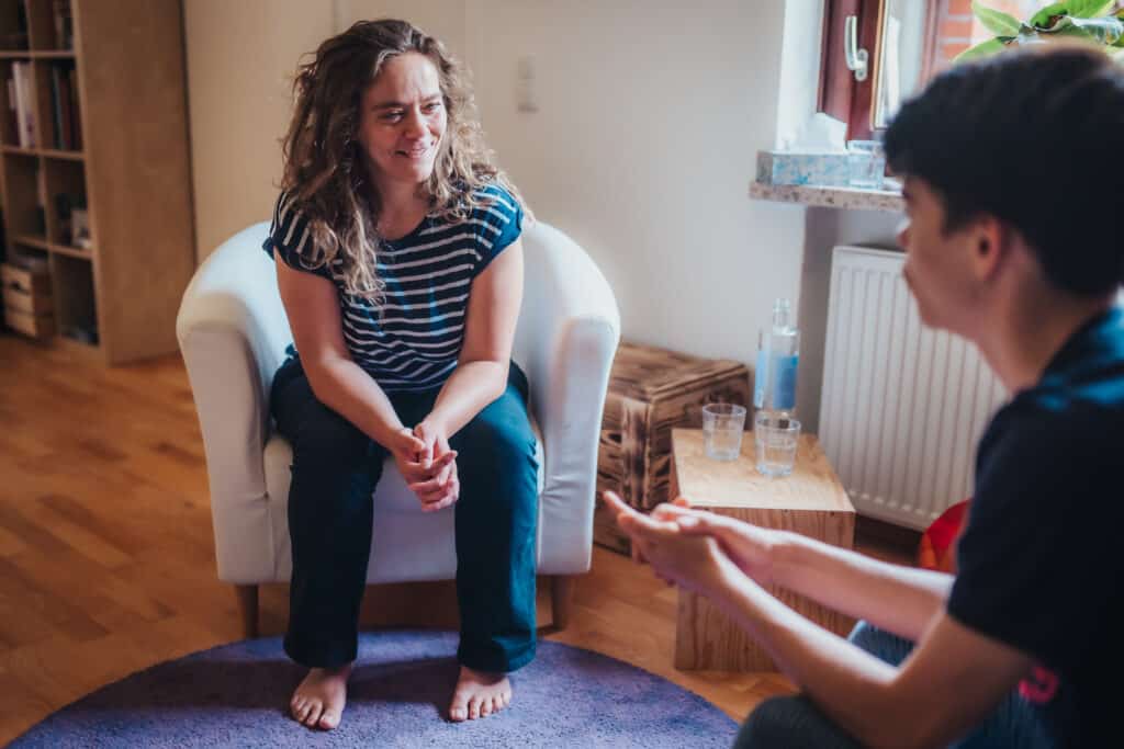 Claudia Hannemann, Reflexintegrationstrainerin, sitzt im Gespräch mit einem Coachee. Im Hintergrund ist der Raum ihrer Praxis zu erkennen.
