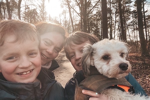 Glück im Alltag: Zwei Jungen, eine Frau - Claudia Hannemann, Gründerin der Awesome Academy - und ein kleiner Hund machen ein fröhliches Selfie bei einem Spaziergang im sonnigen Wald.