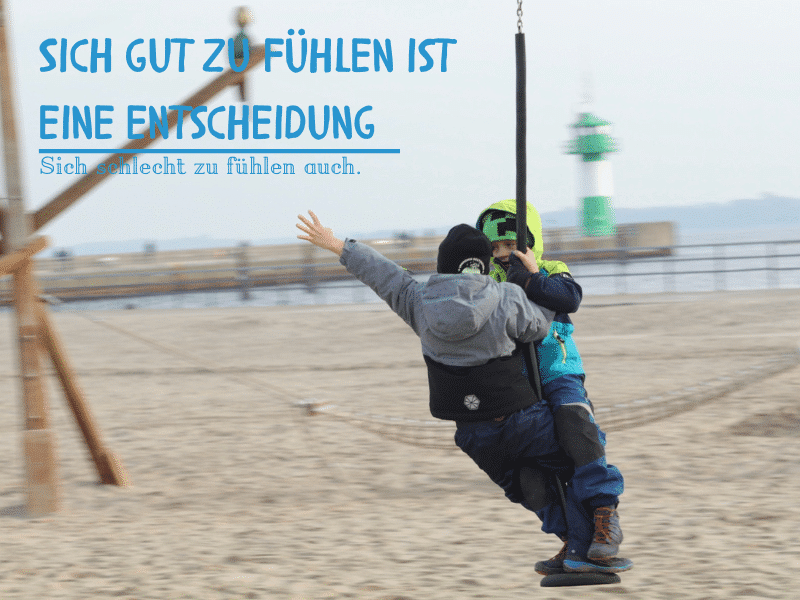 Zwei Kinder schaukeln am Strand und lachen – ein Moment des Glücks. Text im Bild: ‚Sich gut zu fühlen ist eine Entscheidung. Sich schlecht zu fühlen auch.