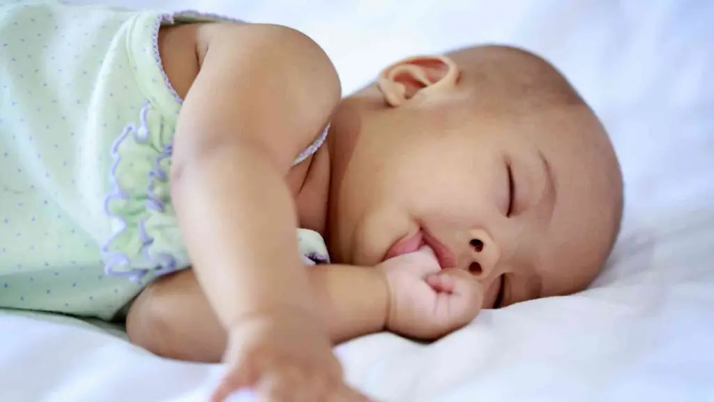 Baby nuckelt im Schlaf am Daumen – der Saugreflex ist einer der frühkindlichen Reflexe, die orale Gewohnheiten im Erwachsenenalter beeinflussen können